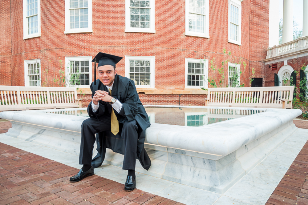 A young grad sits and smiles on the edge of a fountain near UVA's rotunda during a grad photoshoot