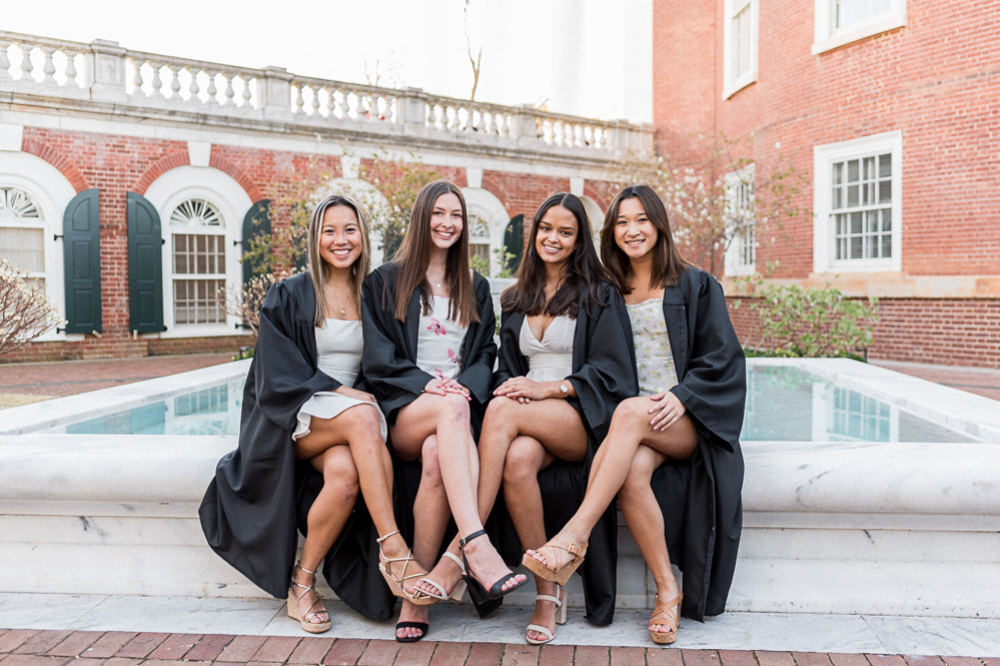 Four girls dressed in their UVA graduation gowns sit on the fountain near the Rotunda