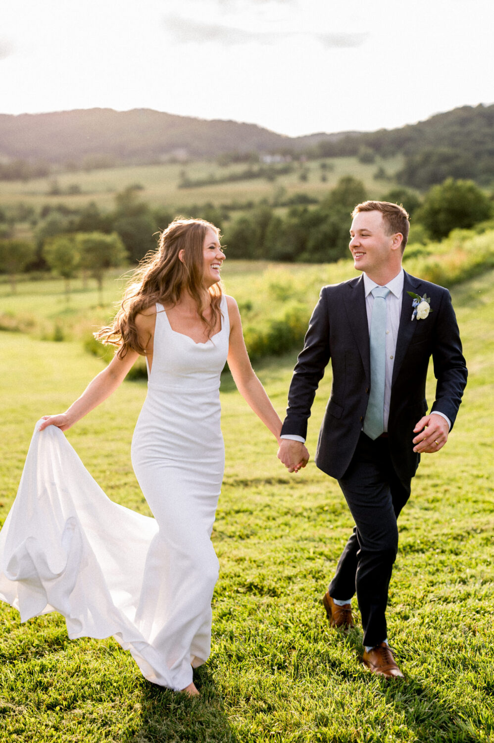 A couple holds hands and grins at each other as they skip through a field at Pippin Hill Farm and Vineyard during their spring wedding