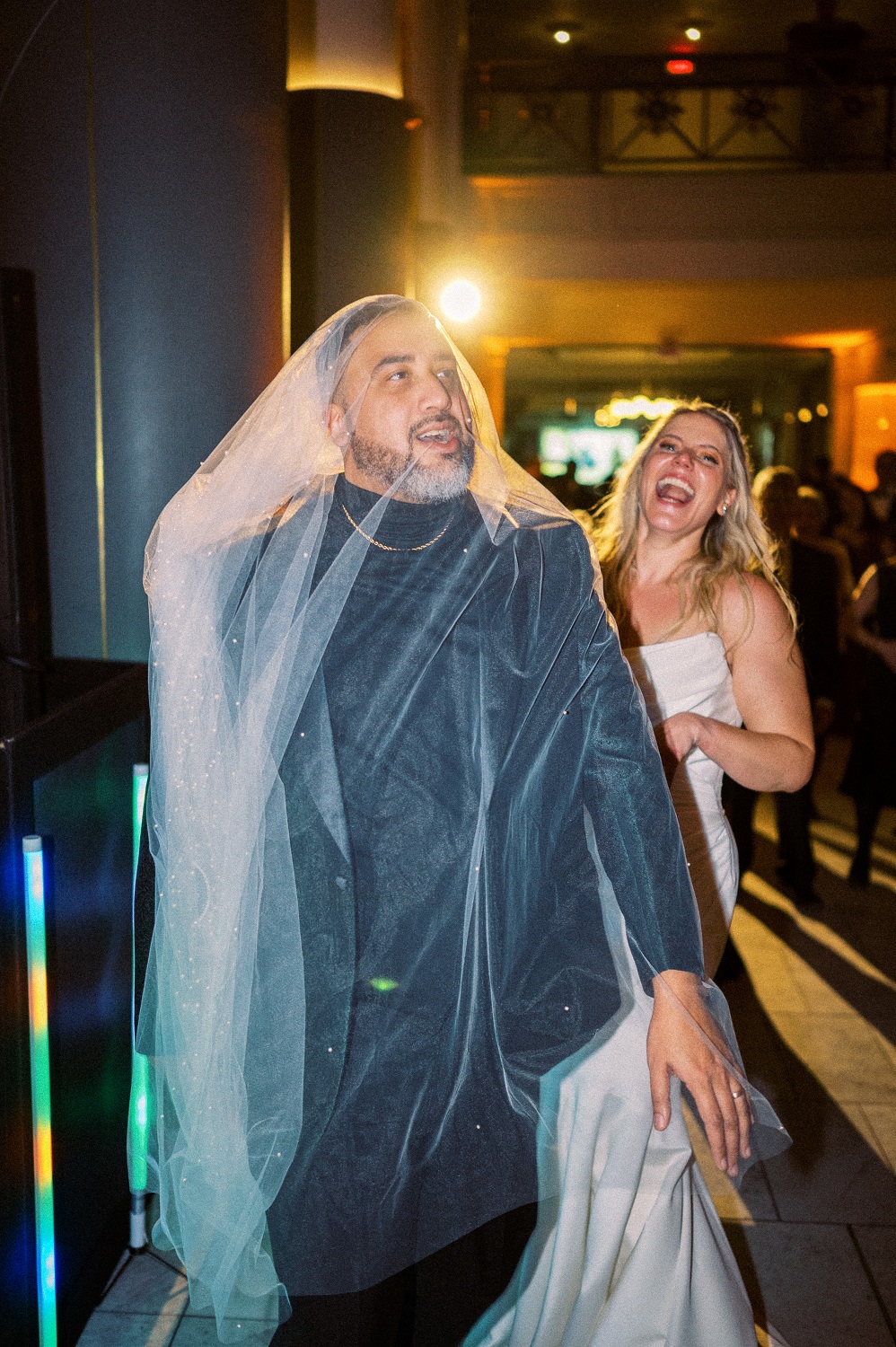 A bride in a white dress laughs at her groom on the dance floor as he gets tangled up in her veil -- captured by Hunter and Sarah Photography during a New Year's Eve Wedding in downtown Charlottesville, VA