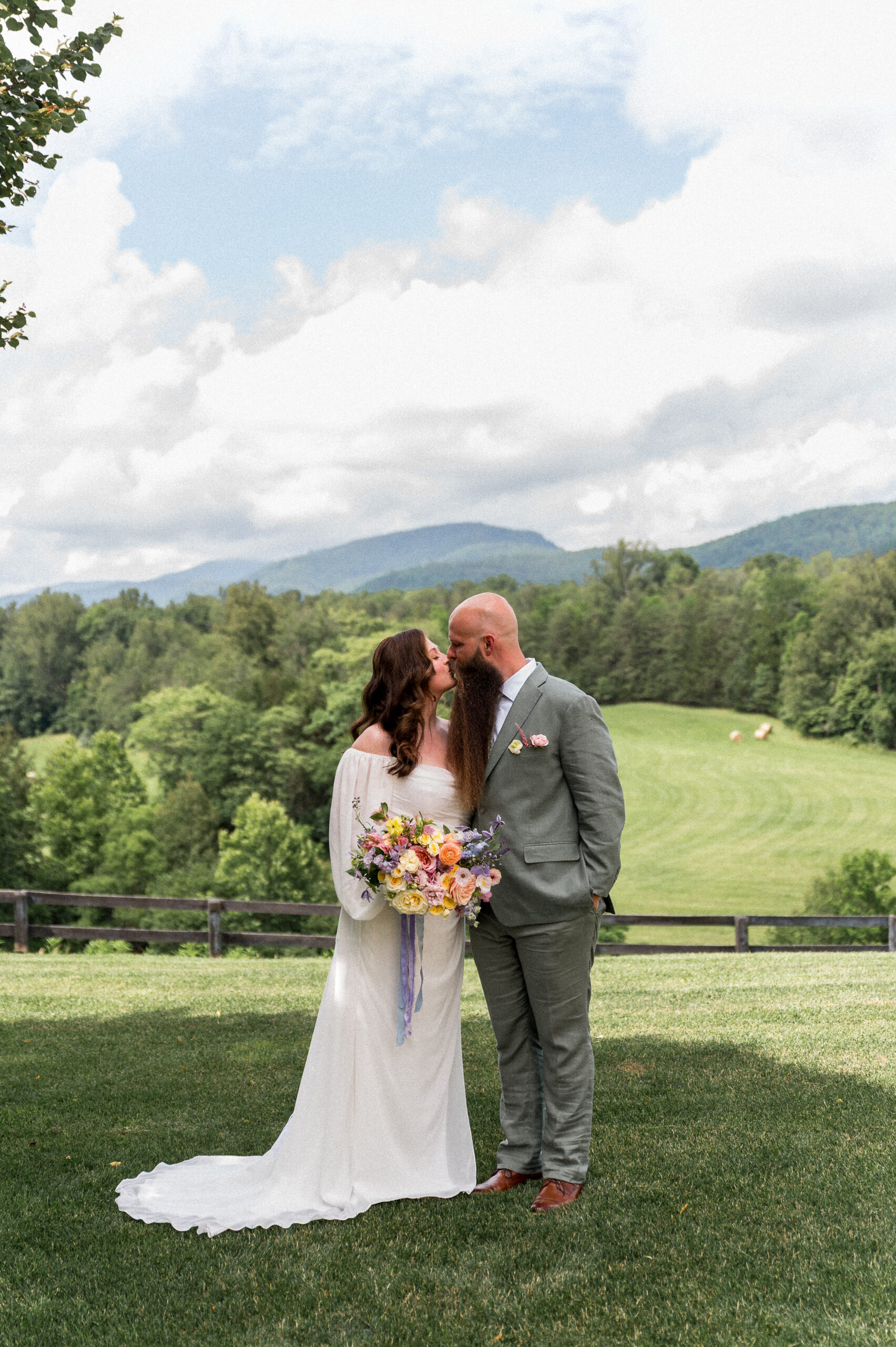 A bride in a bohemian white dress and a groom in a sage green suit kiss on their wedding day during their private estate wedding, beautifully photographed by Hunter and Sarah Photography.