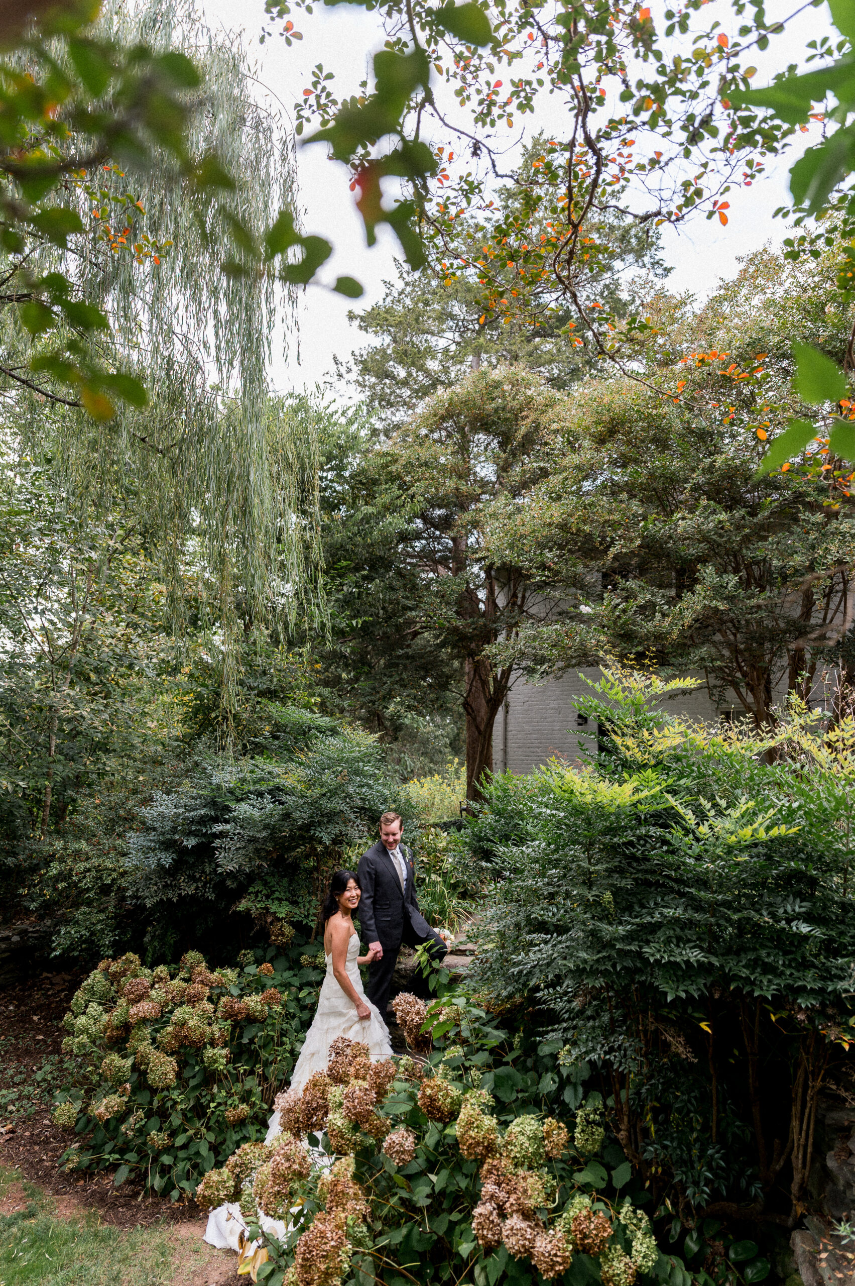 A Korean woman and a white man hold hands amidst hydrangea flowers during their intimate micro-wedding at the Clifton Inn in Charlottesville, VA -- beautifully captured by Hunter and Sarah Photography