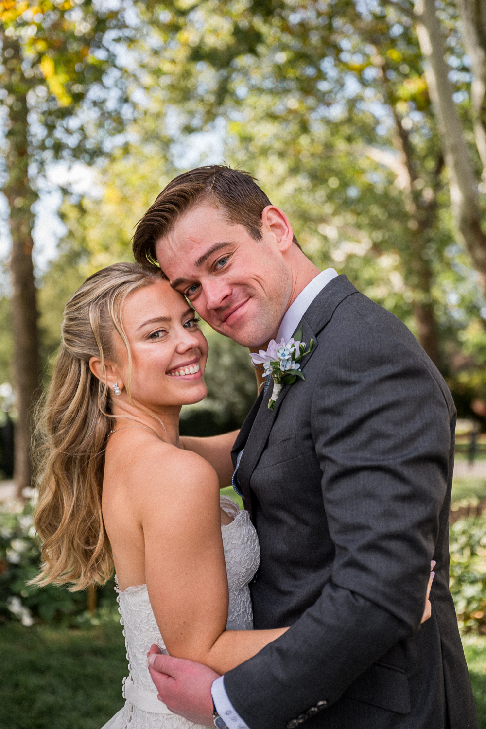 A bride in a white dress and her groom in a grey suit embrace and smile at the camera during their Joyful Fall Farmington Country Club Wedding. Their day was captured by Hunter and Sarah Photography.