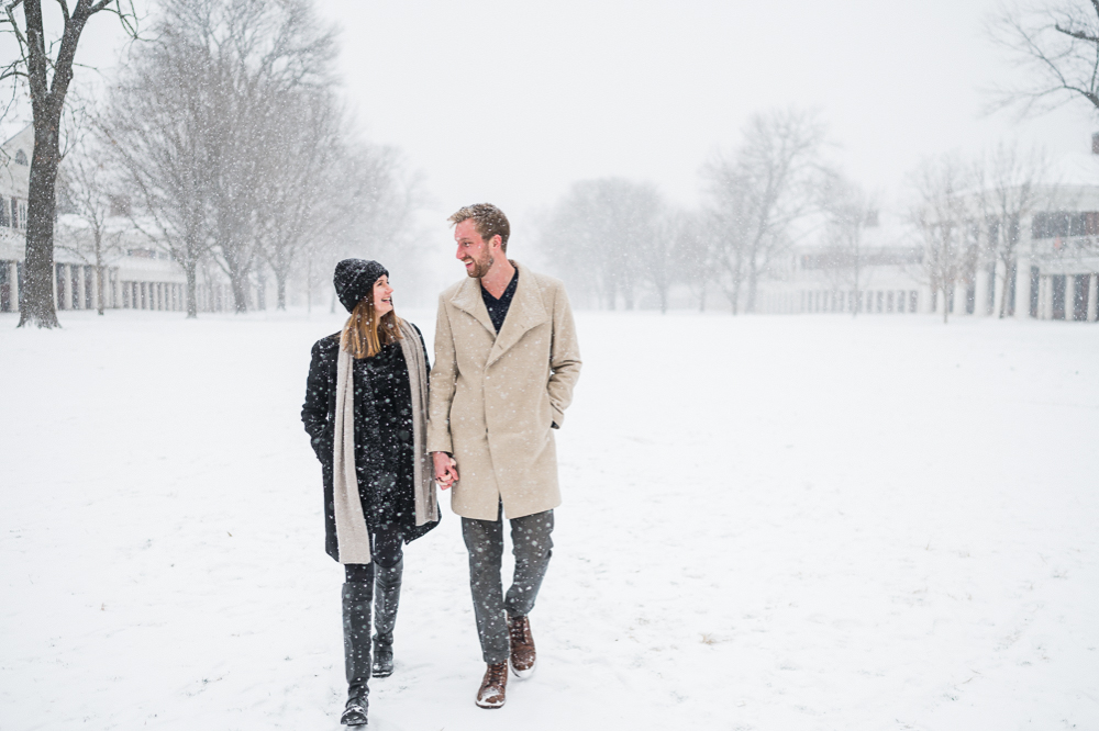 A couple walks down UVa's Lawn in near-blizzard conditions. They're laughing and holding hands, dressed up in peacots and scarves for their engagement photos