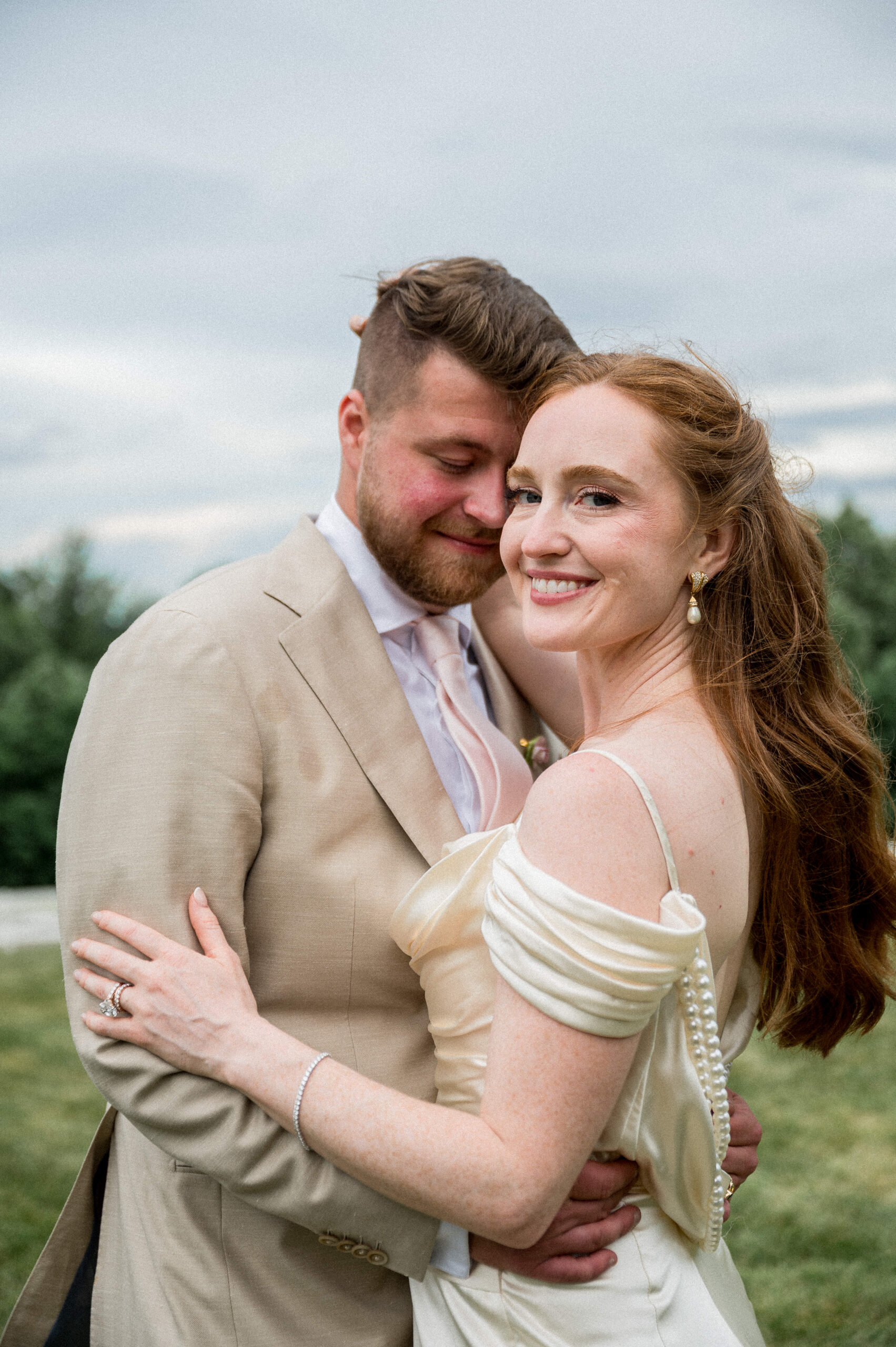 A redheaded bride in a silky backless wedding dress embraces her groom on their wedding day outside Charlottesville, VA
